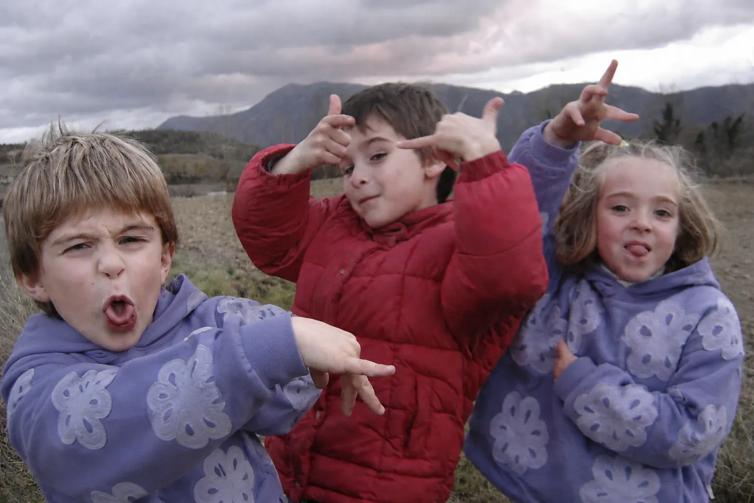 Tres niños con sudaderas NONI de estampado girasol ante un cielo encapotado