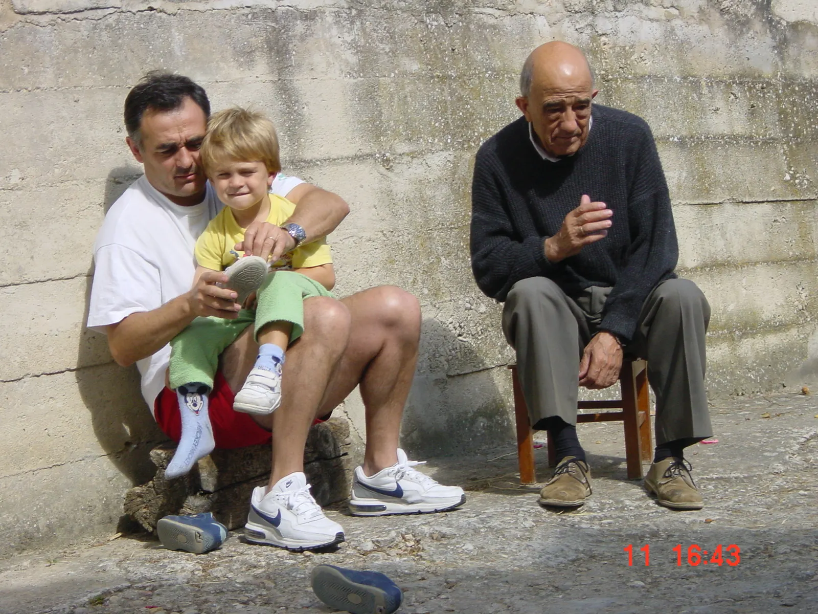 Tres generaciones sentadas al sol contra el muro del pueblo