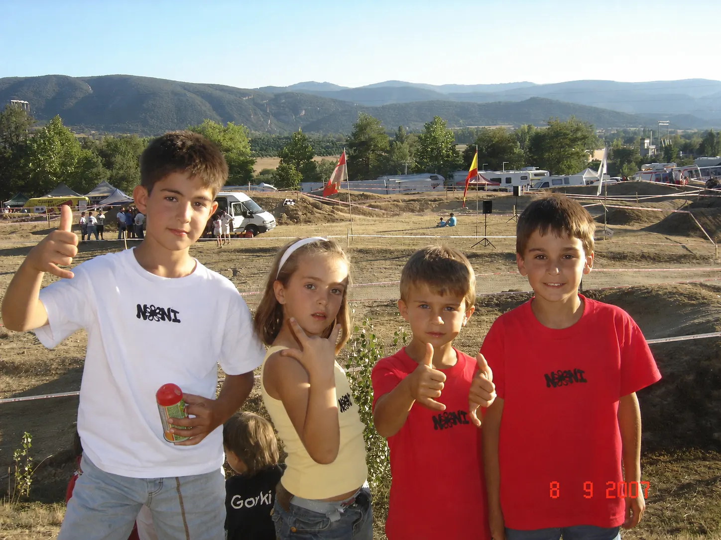 Cuatro niños con camisetas NONI levantan el pulgar ante las montañas del Valle de Tobalina a la luz dorada del atardecer.